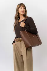 Bolso tipo tote de color marrón, confeccionado en material símil cuero texturado. Presenta un diseño estructurado con asas largas para llevar al hombro y el logo de la marca aplicado en la parte frontal.