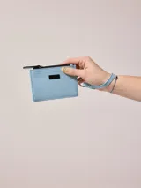 Billetera de poliuretano color celeste, con cierre de cremallera y correa de mano.
