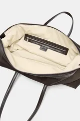 Bolso de hombro con diseño alargado confeccionado en nylon de color marrón oscuro. Presenta doble asa de mano en material a contraste, cierre superior con cremallera metálica y botones laterales decorativos.