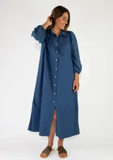Vestido largo azul de corte camisero, con cierre frontal de botones, cuello camisero, mangas largas abullonadas con bordados tonales y diseño holgado.