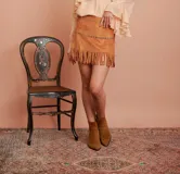 Minifalda color camel de gamuza con flecos en el ruedo y tachas plateadas en la cintura.