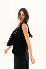 Chaleco oversize de cuero descarne color negro, con diseño de terminación en picos, flecos en la espalda y detalle de tachas metálicas a lo largo de los bordes frontales.