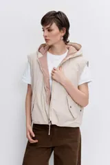 Chaleco reversible con capucha, diseño acolchado con costuras onduladas, cierre frontal y bordes en contraste. Presenta un lado en tono rosado y el otro en tono beige.