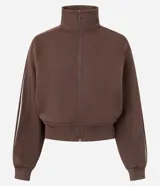 Campera deportiva femenina color marrón, ligeramente cropped, con cuello alto y cierre frontal de cremallera invisible. Presenta mangas largas con detalles contrastantes en blanco, puños y bajo con acabado.