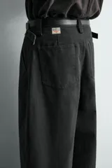 Pantalón de corte relajado confeccionado en tejido de algodón. Presenta cintura con trabillas laterales ajustables, bolsillos frontales y traseros, y un diseño distintivo de costuras laterales giradas que recorren la pernera.