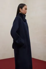 Abrigo largo de lana reciclada en color azul marino, con diseño de cuello alto, mangas raglán y cinturón ajustable a la cintura. Presenta un corte elegante y minimalista con cierre frontal oculto.