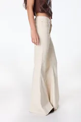 Pantalón de jean azul oscuro, corte acampanado (flare) de tiro alto, con costuras visibles en contraste y bordados tonales en la parte inferior de las piernas. El ruedo es deshilachado.