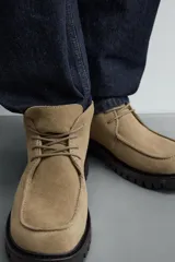 Bota de caña baja con cordones, confeccionada en piel con acabado de serraje. Presenta horma redonda, detalle de costura en el empeine y suela track con volumen.