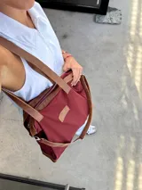 Bolso tipo tote de cuero color bordó con detalles en marrón. Tiene doble asa de hombro, cierre superior y bolsillo interno.