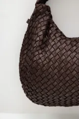 Bolso tipo hobo de cuero marrón oscuro, con diseño trenzado y asa integrada al hombro.