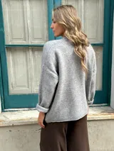 Sweater de punto color gris, de corte holgado, cuello redondo y mangas largas con puños doblados.