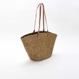 Bolso tipo capazo color kaki, confeccionado en tejido trenzado efecto rafia, con doble asa larga de hombro en cuero sintético marrón claro con costuras blancas visibles.