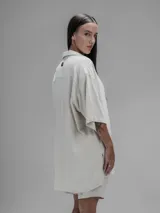 Camisa de corte oversize en color beige, confeccionada en tejido de lino y algodón. Presenta cuello clásico, cierre frontal con botones y mangas cortas amplias.