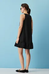 Vestido corto de lino color beige, de silueta suelta y sin mangas, con escote en V decorado con un botón, bolsillos laterales y detalle de volado en el ruedo.