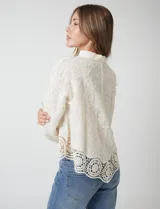 Camisa de algodón con bordado suizo, cuello con solapa y cierre frontal con botones. Presenta mangas largas con terminación de encaje calado y un ruedo asimétrico en pico con un amplio galón de encaje.