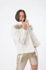 Campera de jean color crudo con cuello alto y apliques de galones dorados y plateados en cuello y hombros.