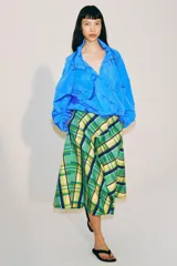 Falda midi de tiro medio marca ZWE Collection, confeccionada en hilatura de algodón con diseño de cuadros tipo tartán en tonos verdes, azules y amarillos. Tiene corte evasé y cierre lateral con cremallera oculta.