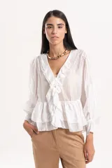 Blusa de tejido liviano color blanco, con escote en V y volados frontales. Presenta mangas largas amplias con puños fruncidos y un volado en el ruedo que le otorga un calce fluido y cómodo.