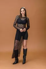Vestido largo de encaje negro con transparencias, manga larga y cuello redondo. Presenta un diseño con tajo lateral profundo que deja al descubierto la pierna.