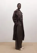 Chaqueta larga tipo gabardina color marrón oscuro, de diseño recto, con solapas amplias y cinturón ajustable del mismo tejido.