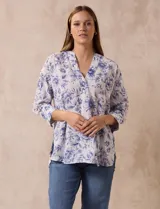 Blusa estampada con flores azules sobre fondo blanco, marca Floral & Ivy. Tiene cuello a la base con escote en V y aplique de botones. Las mangas son tres cuartos con puño y botón. Presenta tajos en las costuras laterales.