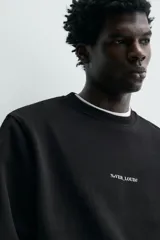 Sudadera de cuello redondo y manga larga, confeccionada en algodón con interior afelpado. Presenta un diseño de corte regular con estampado de texto en contraste en la parte frontal y acabados en rib en puños y ruedo.