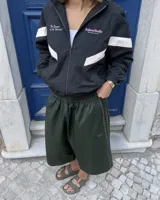 Campera deportiva negra con cuello alto, cierre frontal completo y diseño oversize. Cuenta con bandas blancas diagonales en las mangas y el torso, y texto estampado en el pecho.