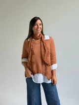 Sweater de punto color naranja con diseño asimétrico, que incluye una bufanda a juego con detalles bordados y una camisa blanca de base integrada.