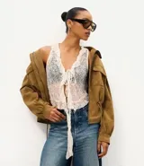 Blusa sin mangas de encaje color crudo, con escote en V, volados en la abertura frontal y cordón ajustable para atar en el pecho.