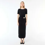 Vestido largo negro de manga corta y cuello redondo, con diseño ajustado y detalle drapeado en la cintura adornado con un aplique metálico dorado.