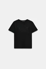 Camiseta de algodón color negro, con cuello redondo y manga corta. Presenta un detalle de bordado floral al tono en la parte frontal.