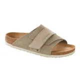 Sandalia Birkenstock modelo Kyoto, confeccionada en gamuza color taupe. Presenta un diseño de una sola correa ancha ajustable con cierre de velcro y detalles de remaches metálicos. Cuenta con la clásica plantilla anatómica de corcho y látex, y suela de EVA.