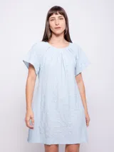 Vestido corto de corte holgado, color celeste, con cuello redondo fruncido y mangas cortas. Está confeccionado en una tela con textura diferenciada que le aporta relieve.