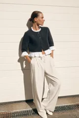 Chaqueta gris de cuello redondo y manga tres cuartos, con detalle de volantes de popelín blanco en el cuello, puños y bajo. Cierre frontal con botones.