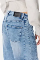 Jean de corte wide leg y tiro medio, con diseño de costuras laterales curvadas que le otorgan una silueta redondeada. Presenta un lavado azul claro con efecto desgastado, cierre frontal con botón y bolsillos laterales.