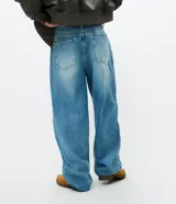 Pantalón de jean corte super baggy, color azul medio, con aplicaciones tribales y recortes desflecados. Cuenta con cintura con pasadores, cierre frontal con botón y cremallera, y bolsillos funcionales.
