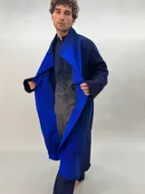 Tapado oversize desestructurado de lana merino afieltrada, teñido en degradé azul y negro. Tiene bolsillos laterales, cierre con broches ocultos y puños amplios que cubren la mano.