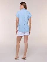 Blusa de diseño recto y textura suave de denim liviano color celeste, con cuello solapa abierto en V, pechera con detalle pespunteado y pliegue central. Presenta mangas cortas caídas con dobladillo fijo y ruedo ligeramente curvo.