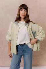 Camisa lila de calce relajado y manga larga, con cuello clásico, puños y bolsillo delantero en denim contrastante. Cierre frontal con broches metálicos.