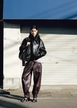 Chaqueta de estilo bomber color negro, confeccionada en 100% piel ovino con acabado de napa y diseño oversize. Cuenta con cuello alto envolvente, manga larga con puños ajustables, cierre delantero oculto con botón magnético y forro interior de poliéster.