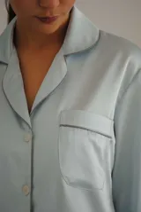 Pijama de satén elastizado color celeste, compuesto por una camisa de manga larga con cuello solapa, botones frontales y bolsillo en el pecho, y un pantalón recto con cintura elástica y lazo ajustable.