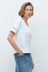 Remera blanca de algodón con cuello en V y mangas cortas que presentan un detalle de puntilla en los bordes.
