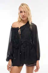 Blusa negra traslúcida con mangas largas abullonadas y detalle de encaje floral en el frente.