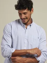 Camisa de manga larga con patrón de rayas verticales celestes y blancas, corte regular fit, cuello con botones y un bolsillo en el pecho con logo bordado.
