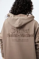 Canguro negro con capucha y bolsillo delantero. Presenta un bordado frontal y trasero con lettering “Mont Saint-Michel”.