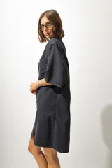 Vestido camisero corto en denim color gris oscuro, de corte holgado, con cuello camisero, manga corta, bolsillo frontal y cierre frontal con botones blancos.