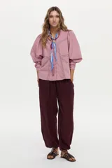 Blusa rosada de algodón liviano, con cuello mao y escote en V, mangas largas abullonadas y detalles de encaje y puntilla en el frente.