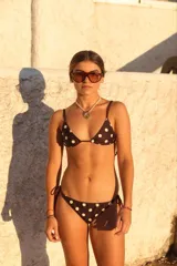 Bikini de dos piezas con estampado de lunares marrones sobre fondo crema. El top es de estilo triangular con tiras finas para atar, y la bombacha es de corte semi-vedetina con tiras laterales ajustables.