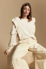 Sweater de manga larga color crema, con volados en el delantero y las mangas. De tejido suave y caída liviana, con silueta recta.