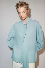 Camisa de rayas finas color amarillo, confeccionada con cuello redondo y lazada en el mismo tejido en el escote. Presenta mangas largas con hombros caídos y puños anchos abotonados.